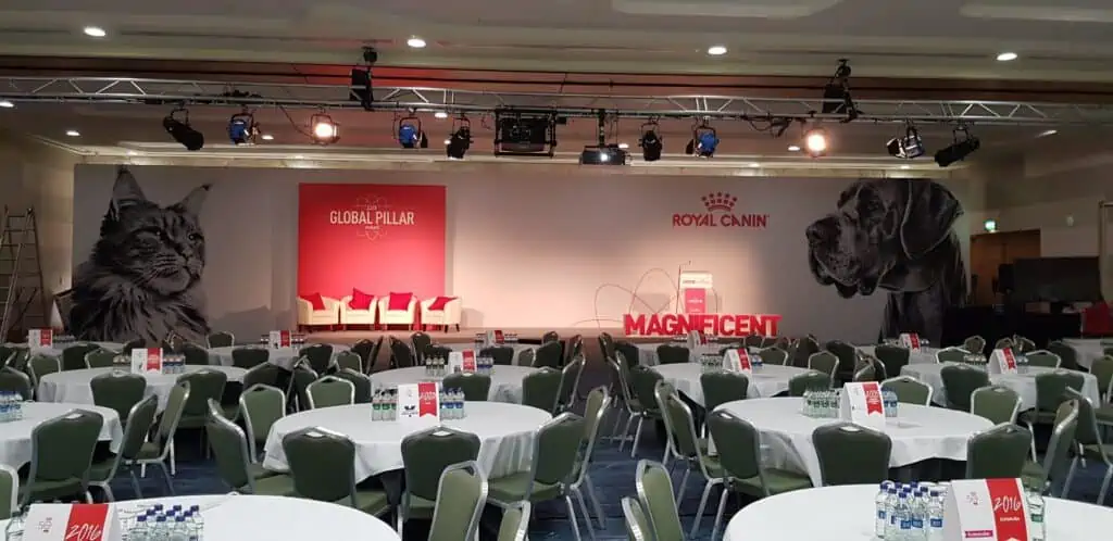 A large conference room with numerous tables and a stage