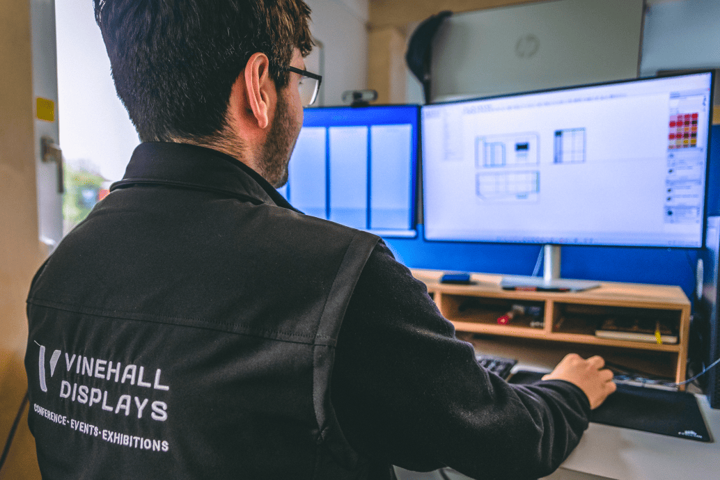 An employee operates a computer, designing an exhibition stand